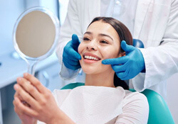 happy dental patient holding mirror looking at her teeth