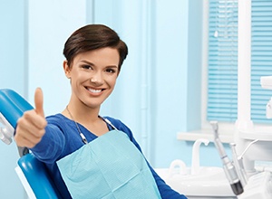 Happy dental patient in blue sweater making thumbs-up gesture